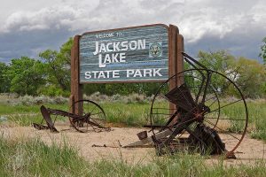Rustic sign in a park with old wagon wheels around it reads "Welcome to Jackson Lake State Park".