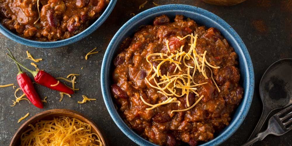 A bowl of chili topped with shredded cheddar next to a red chili pepper