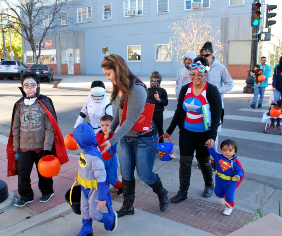Families in costume walking a downtown sidewalk during Trick or Treat Street in Morgan County